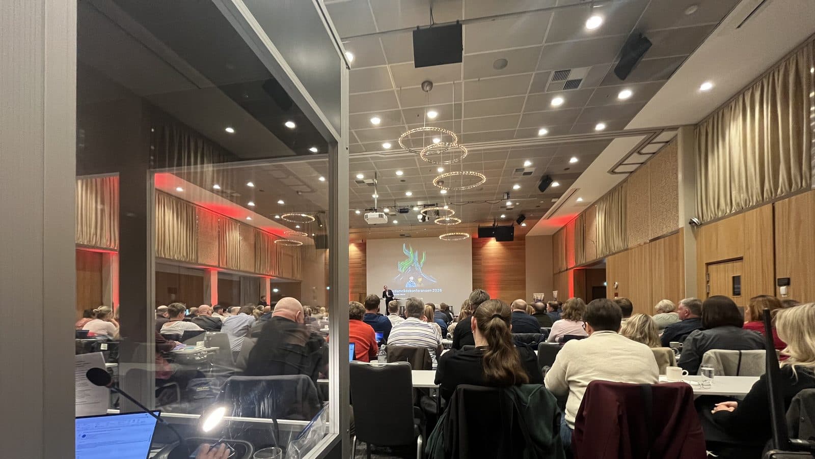 Utsikt fra en tolkekabin ut i en fullsatt konferansesal