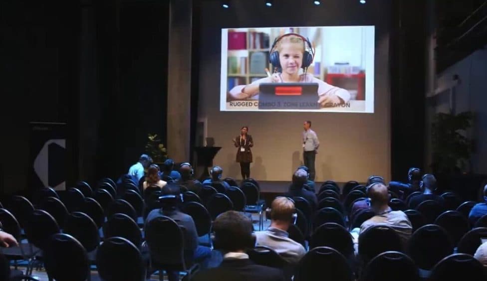 Plenary hall with an audience wearing headsets and a person on the main screen