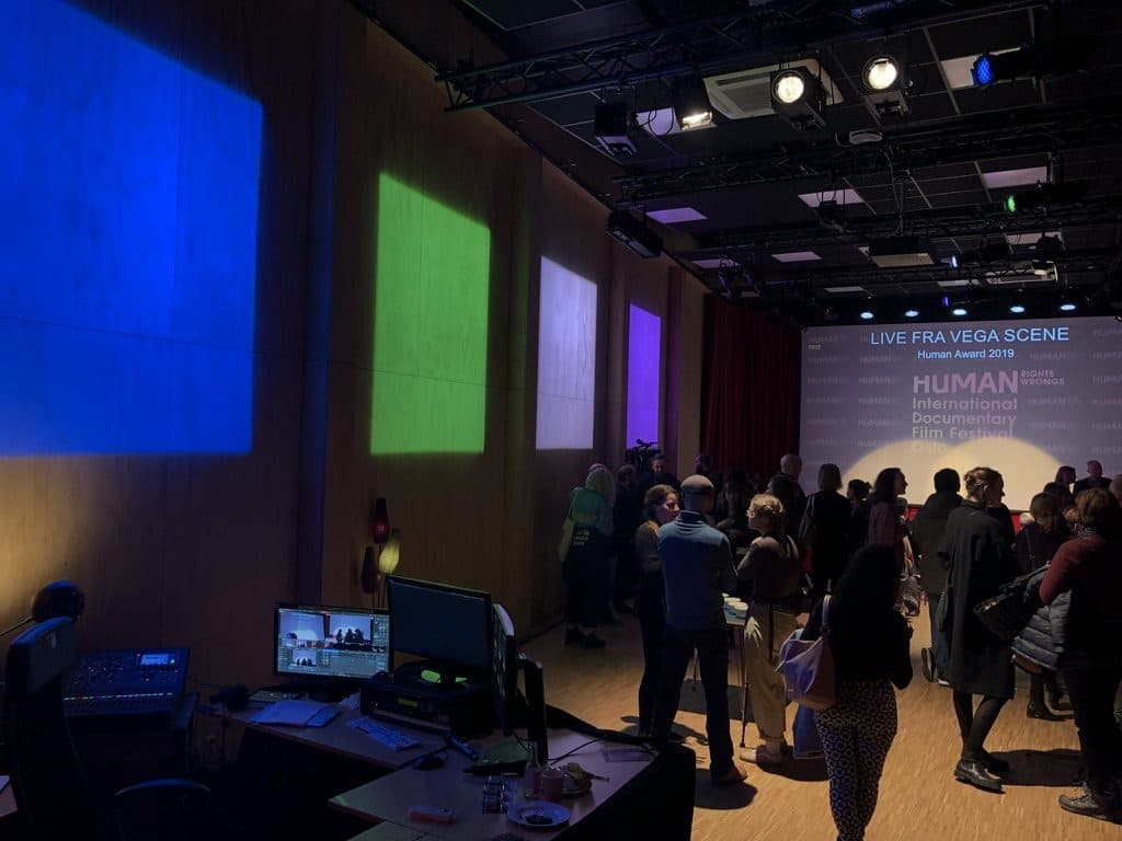 Streaming desk with a mixer and monitors, and an audience in the hall during a festival screening