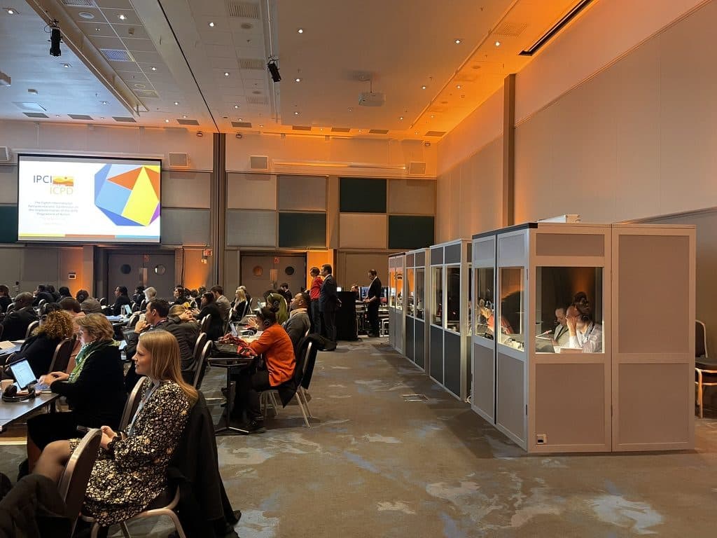 ISO interpreter booths at the back of a conference hall, with delegates wearing headsets at the tables